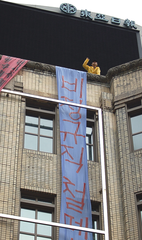 12일 오후 장맛비가 내리는 가운데 한 노동자가 광화문 일민미술관 옥상에서 '비정규직 철폐' 구호가 적힌 플래카드를 펼쳐놓고 구호를 외치고 있다.